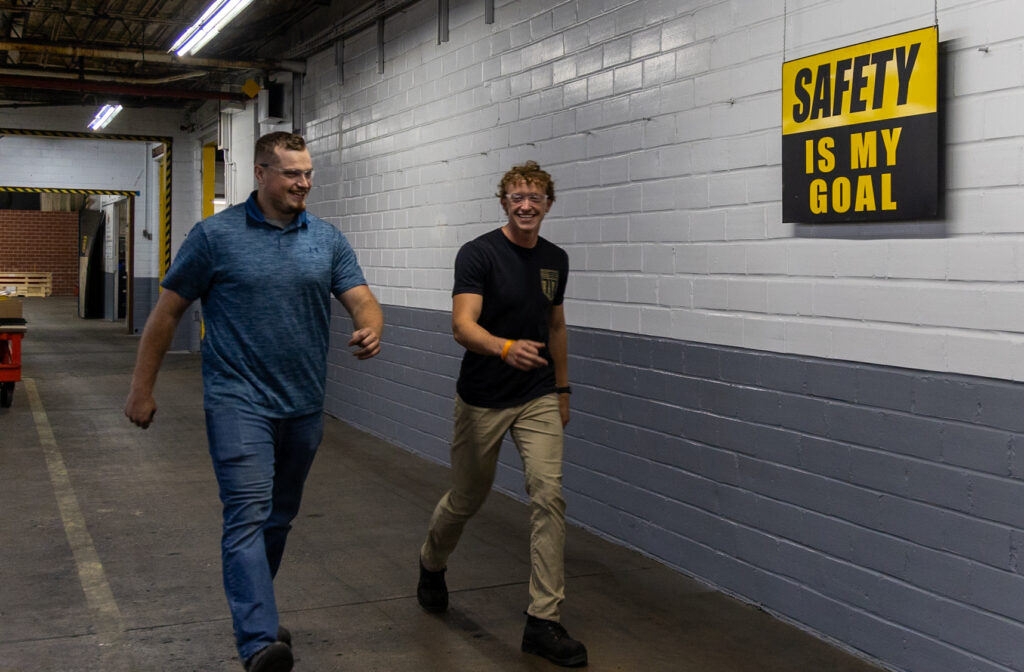 Two male workers in hall by safety sign